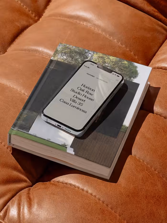 Smartphone displaying a list of project names resting on an architectural book on a brown leather surface.