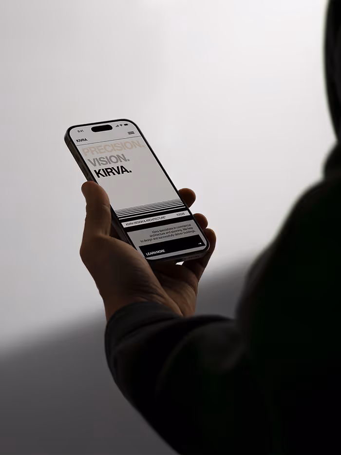 Person holding a smartphone displaying a webpage with the text 'PRECISION. VISION. KIRVA.' and a section about Kirva Design Architecture.