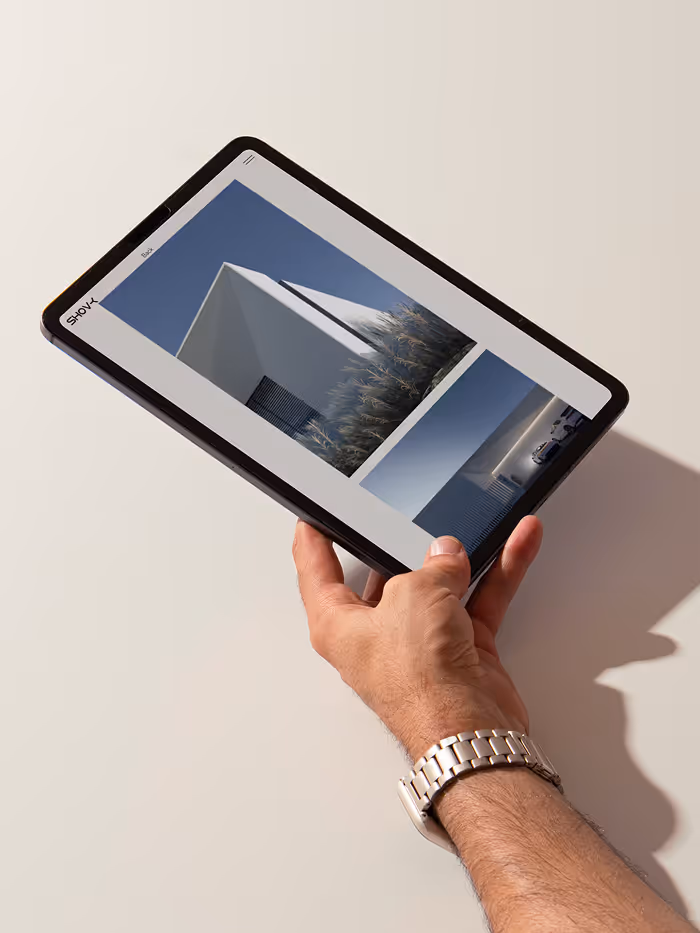 Hand holding a tablet displaying modern architecture photos on a light surface with shadow.