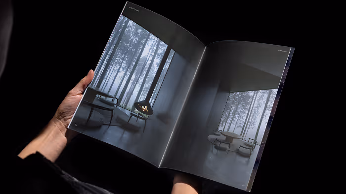 Person holding an open magazine showing images of a modern, minimalist room with large windows and a fireplace.